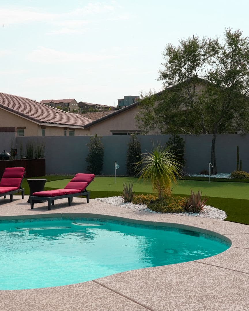 Backyard pool with lounge chairs, putting green, and landscaped garden in a sunny setting.