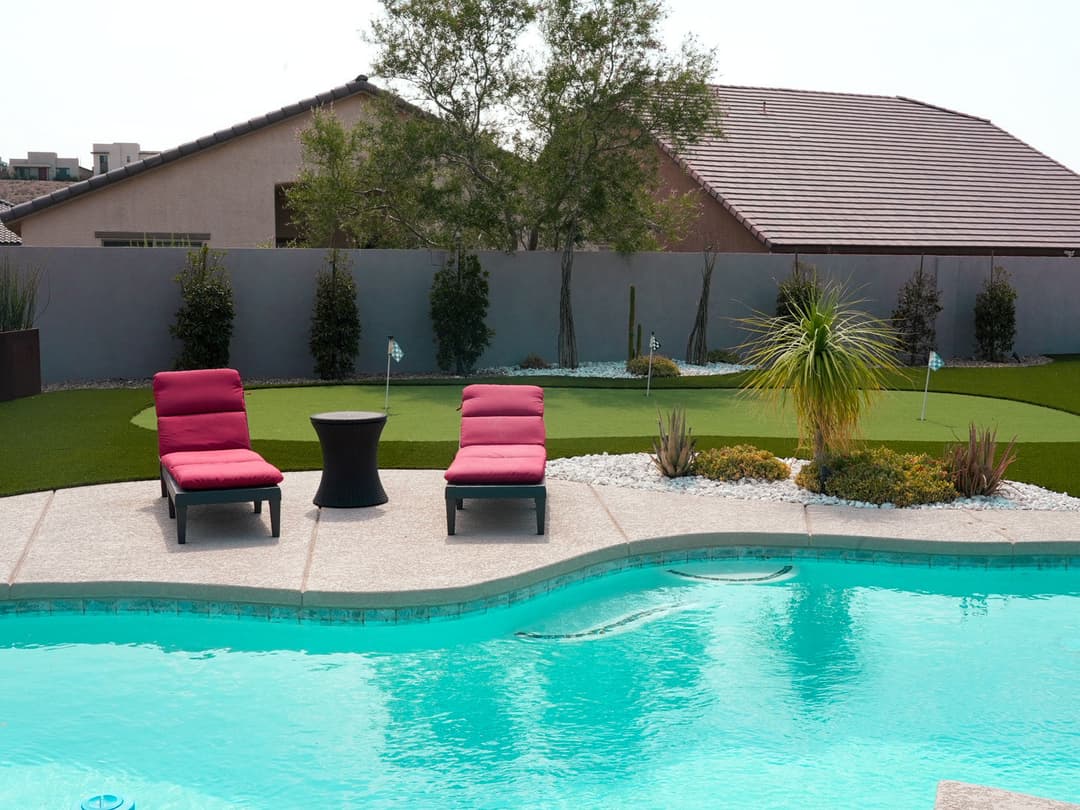 Luxury backyard with a pool, two red lounge chairs, and a putting green.
