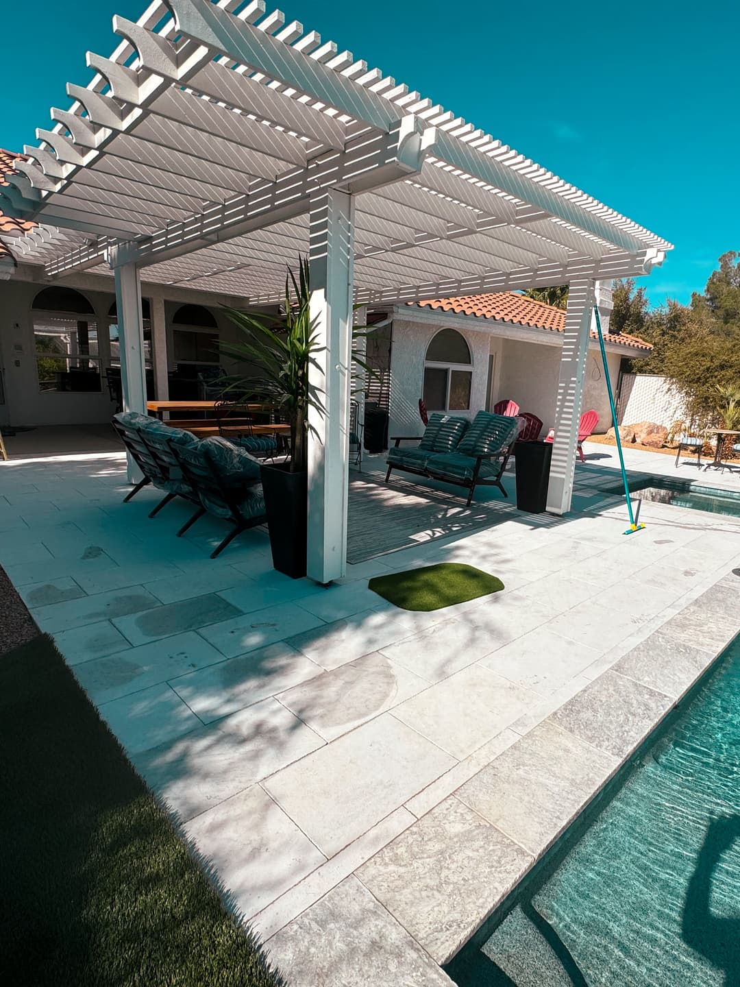 Modern patio area with shaded seating, pool, and lush landscaping in a sunny setting.