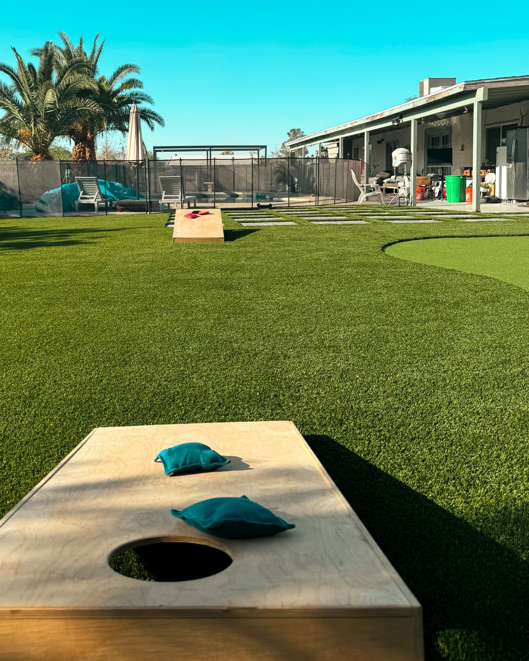 Outdoor cornhole setup with vibrant green turf and a sunny blue sky.