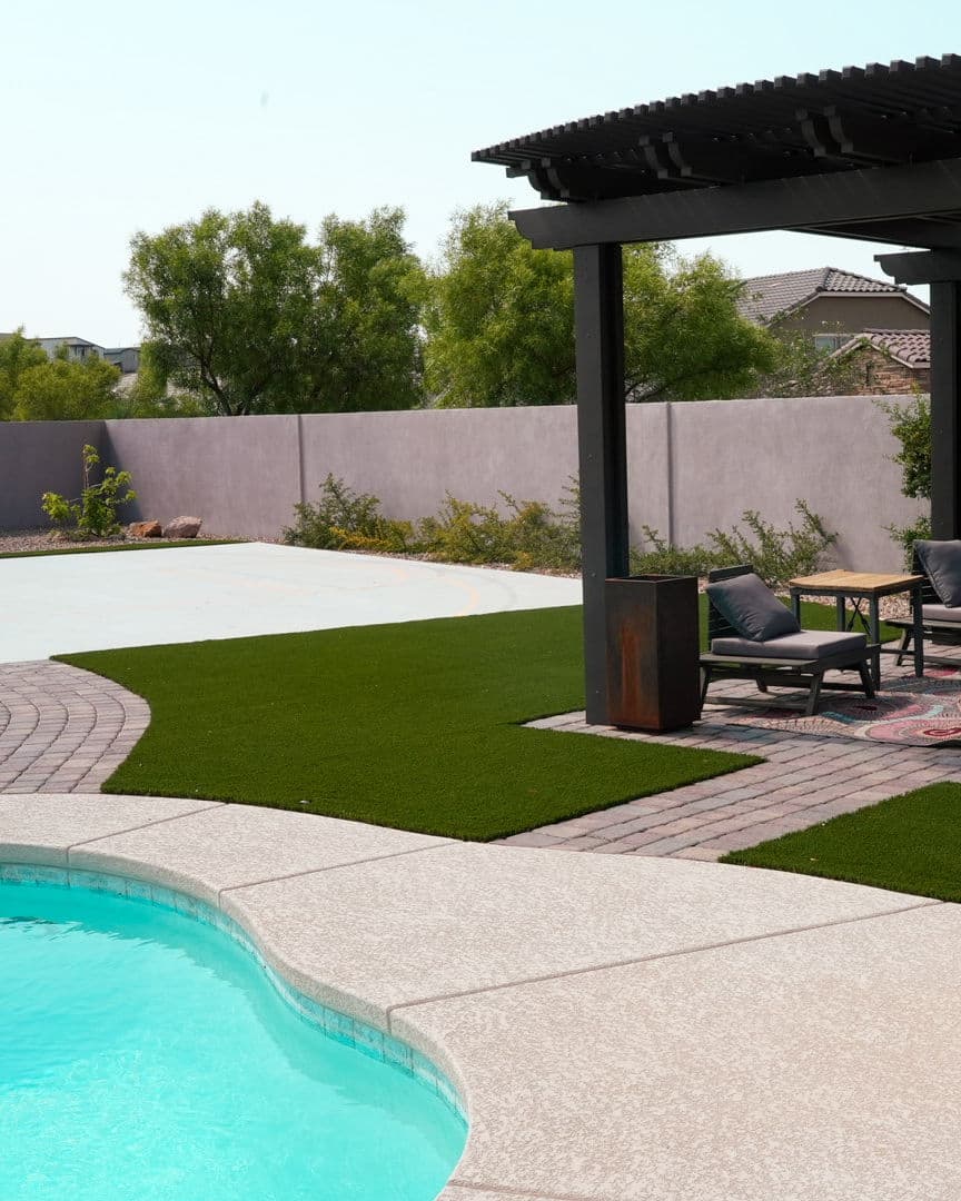 Luxurious backyard with a pool, patio seating, and artificial turf surrounded by greenery.