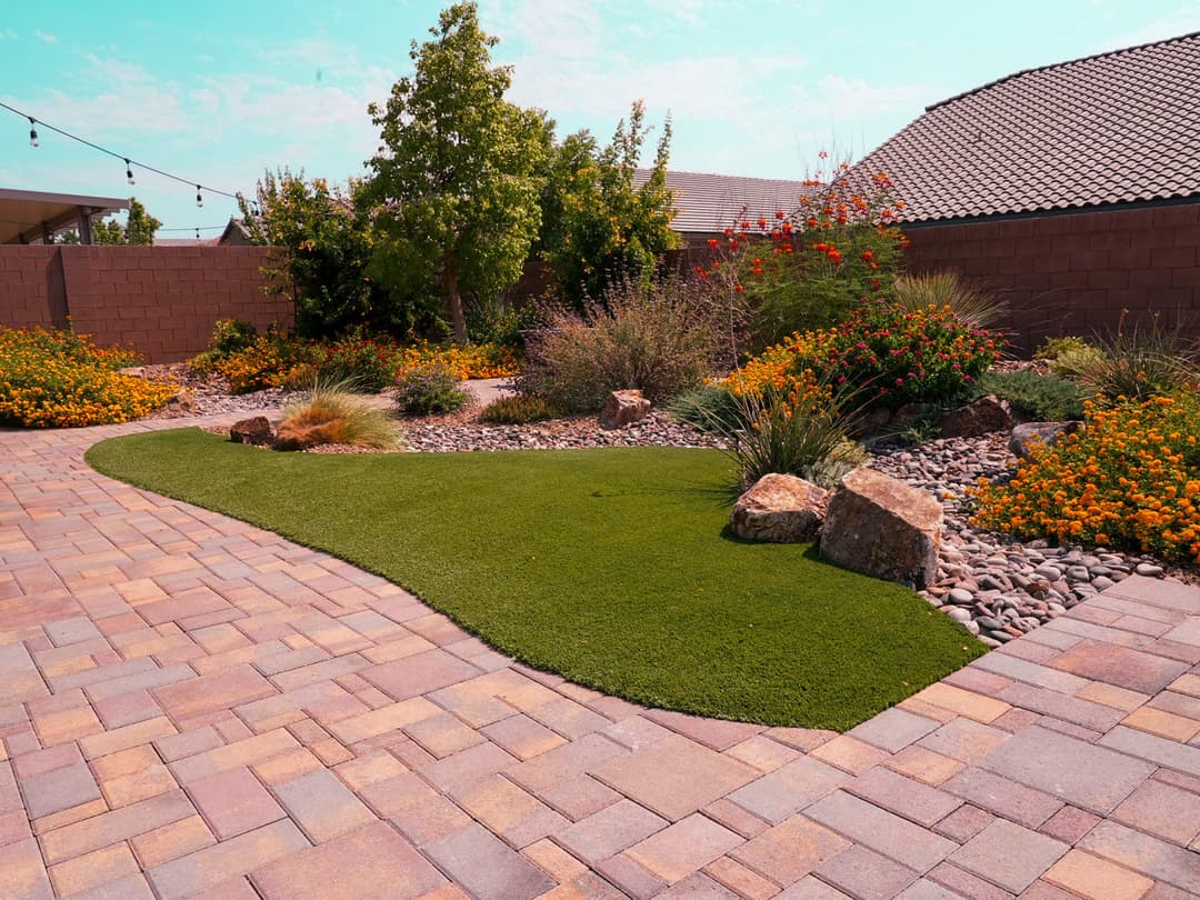 Lush backyard landscape with artificial grass, colorful flowers, and stone pathways.