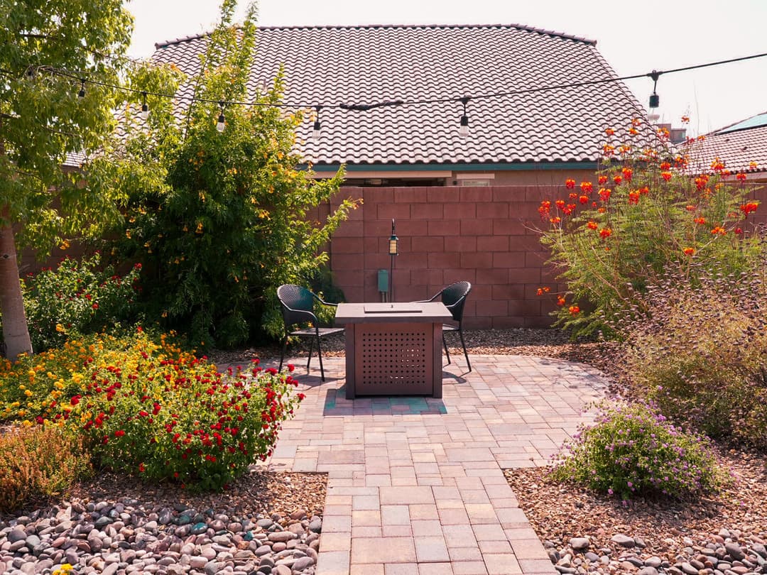 Outdoor patio with a fire pit, seating area, and colorful landscaping in a sunny setting.