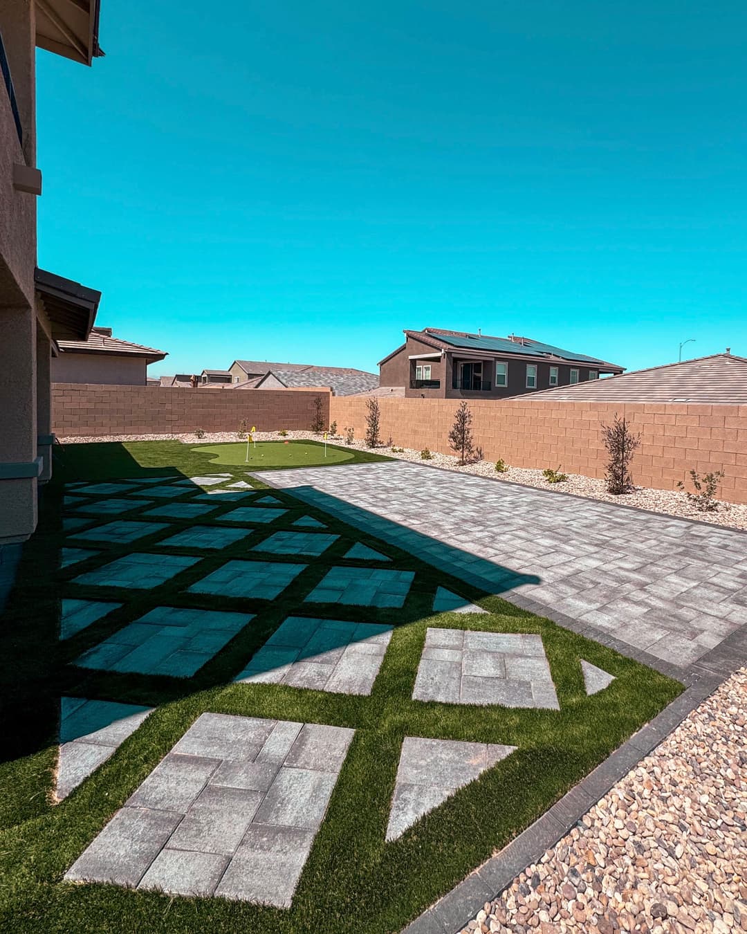 Modern backyard design featuring paved stone patterns, green grass, and clear blue sky.
