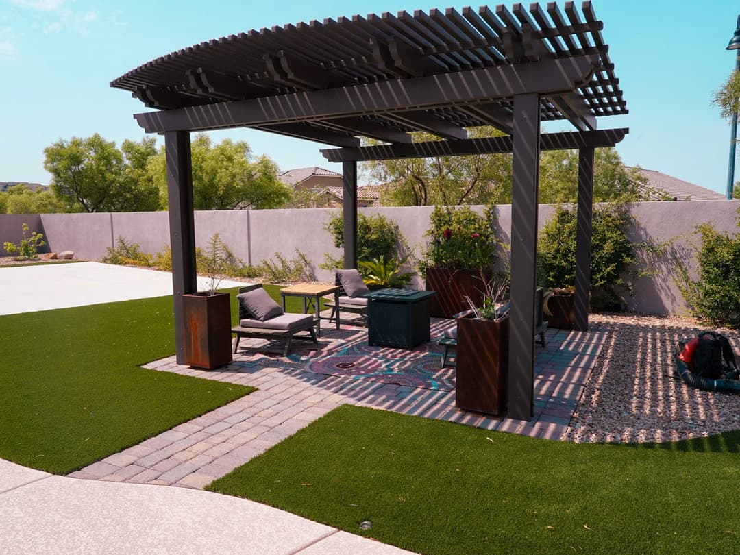 Modern backyard patio with pergola, lounge chairs, and lush green landscaping. Relaxation space.