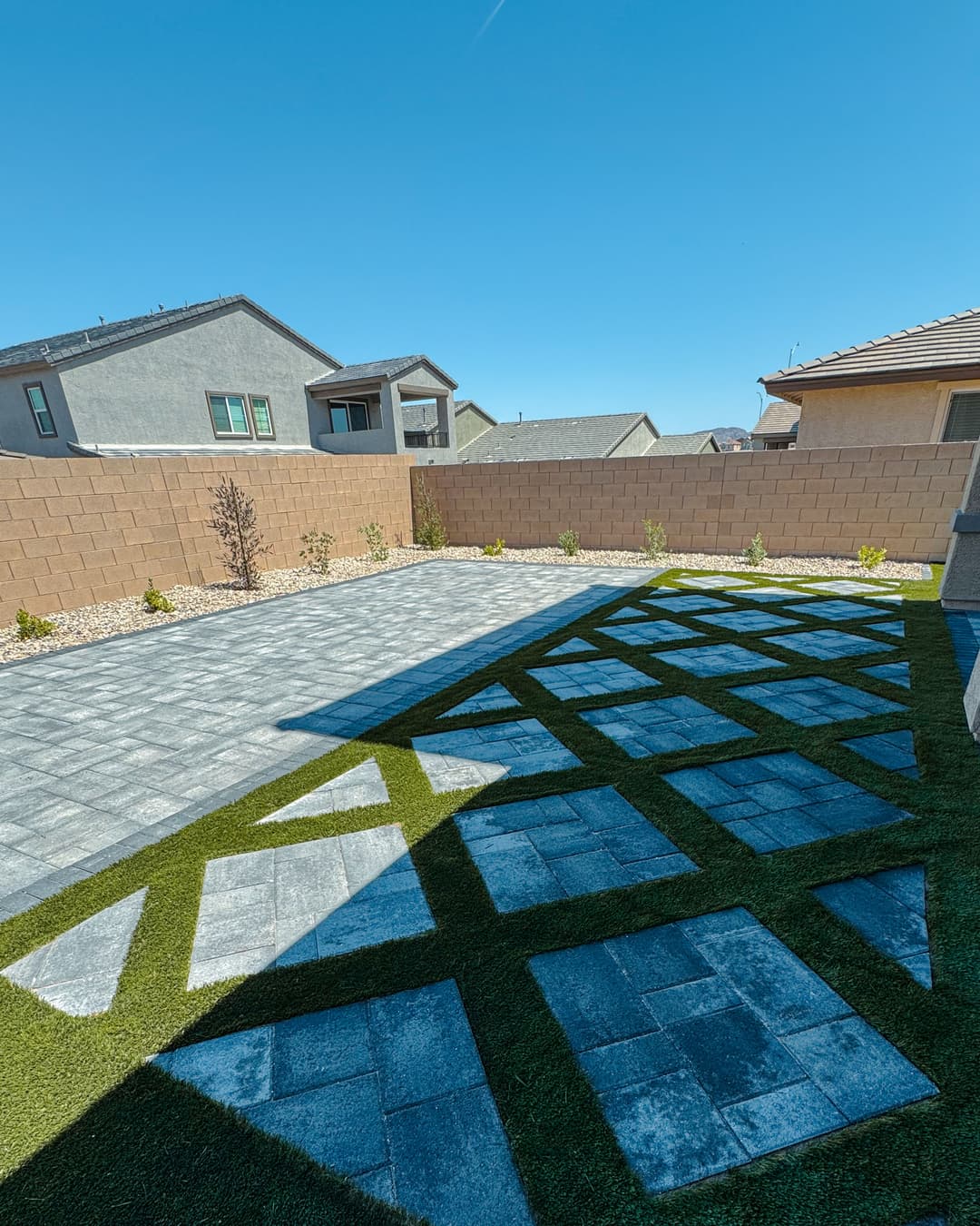 Modern backyard with paved patio, green grass accents, and decorative landscaping.
