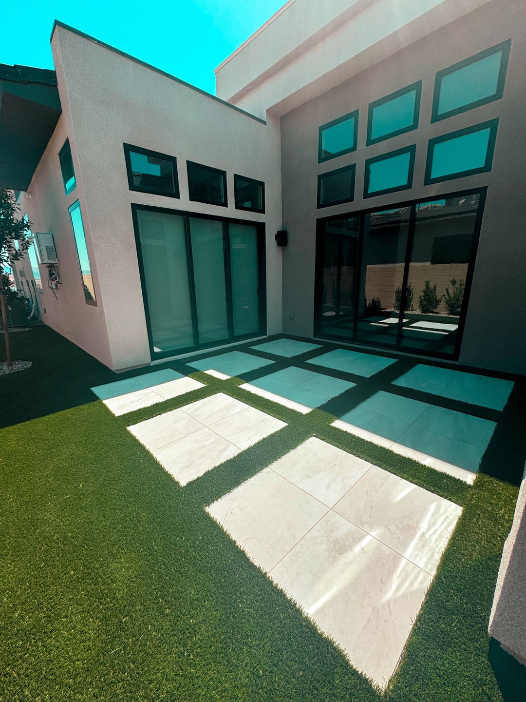Modern home exterior with large windows, patio, and green lawn, featuring sleek marble tiles.