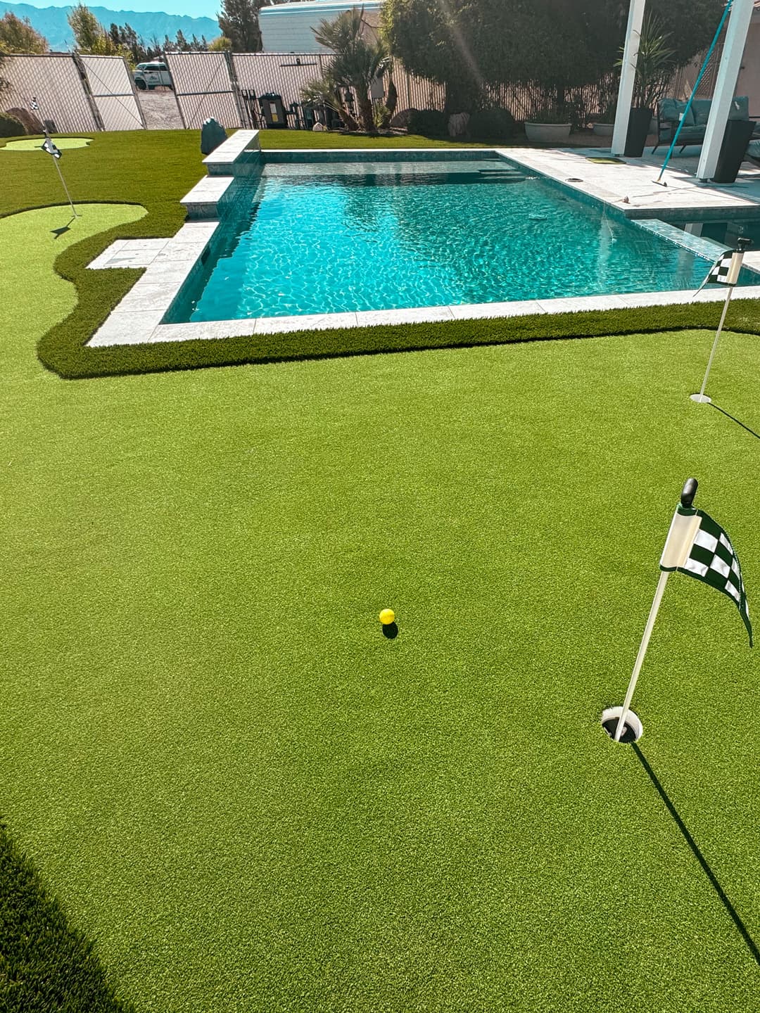 Synthetic putting green near a blue swimming pool, featuring a golf ball and flags.
