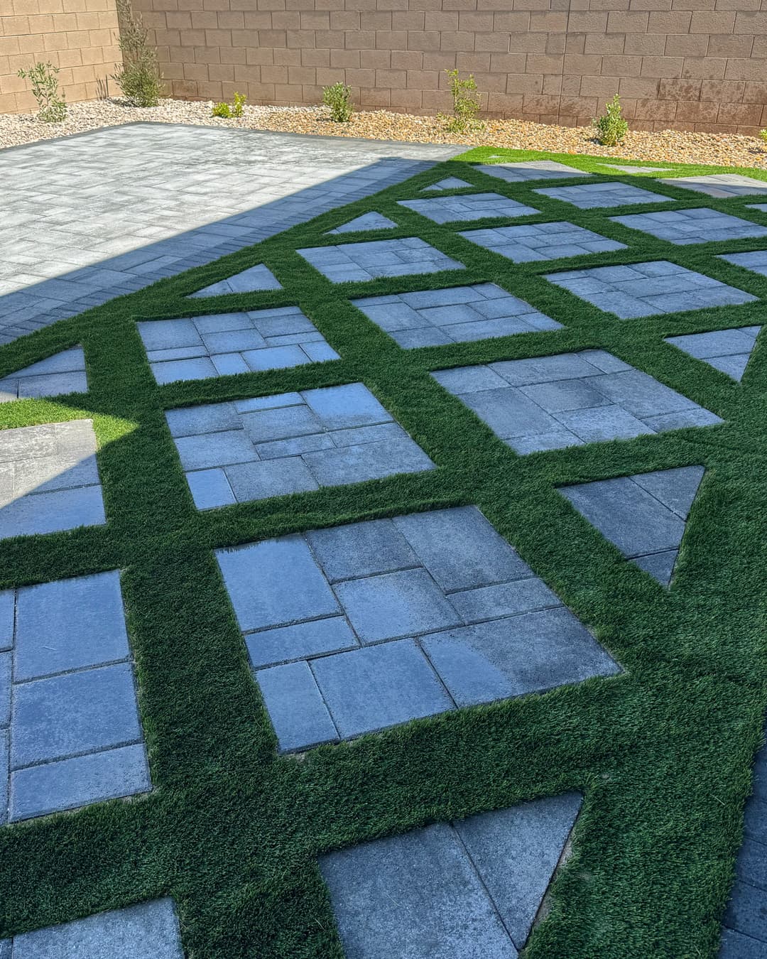Modern patio design with stone pavers and green grass accents in a landscaped yard.