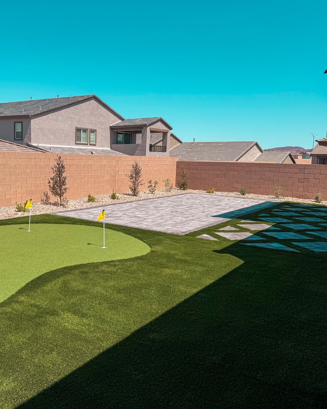 Modern backyard featuring a putting green, paver patio, and landscaped gravel area.