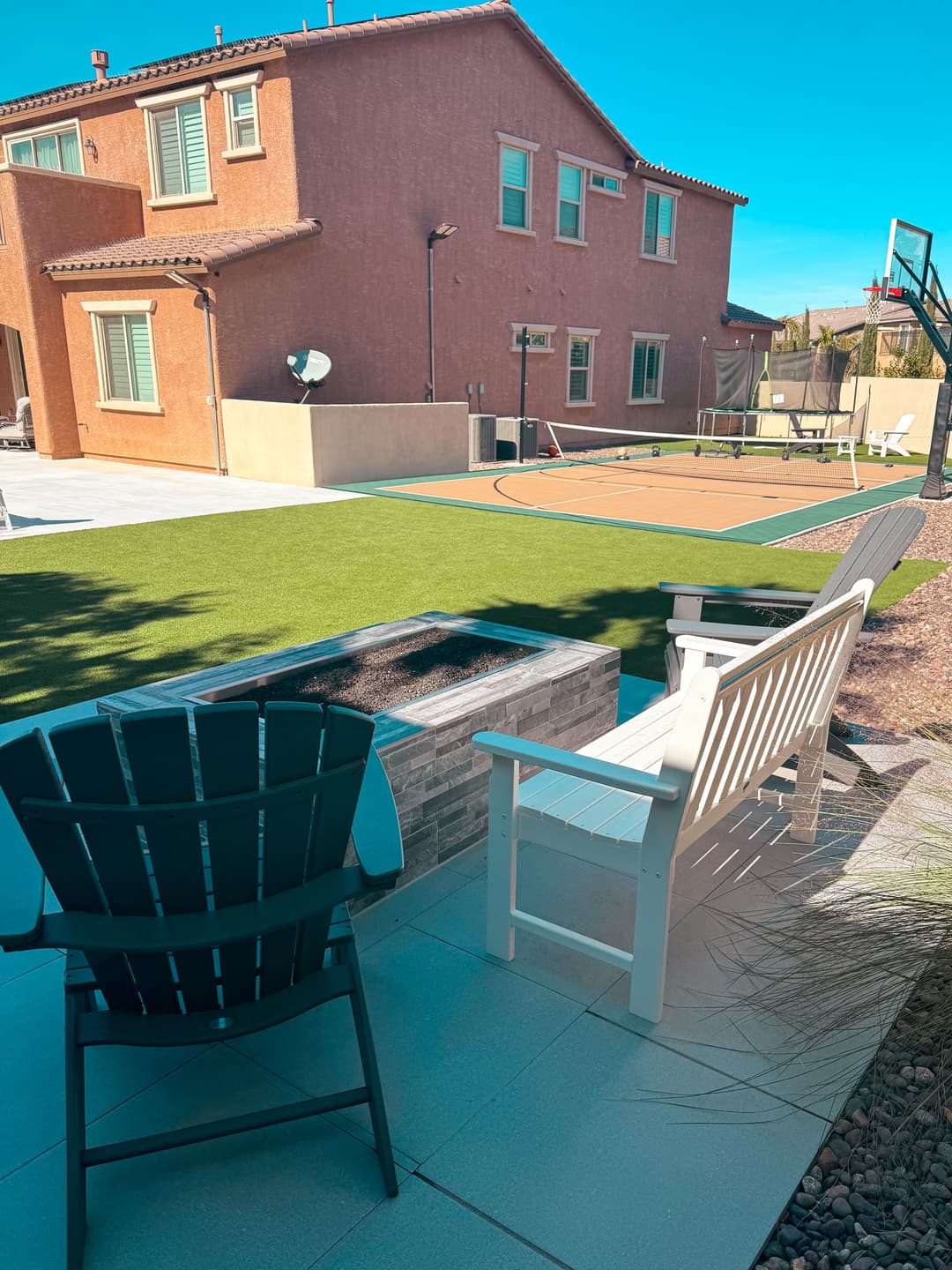 Backyard oasis with seating, fire pit, and basketball court under a clear blue sky.