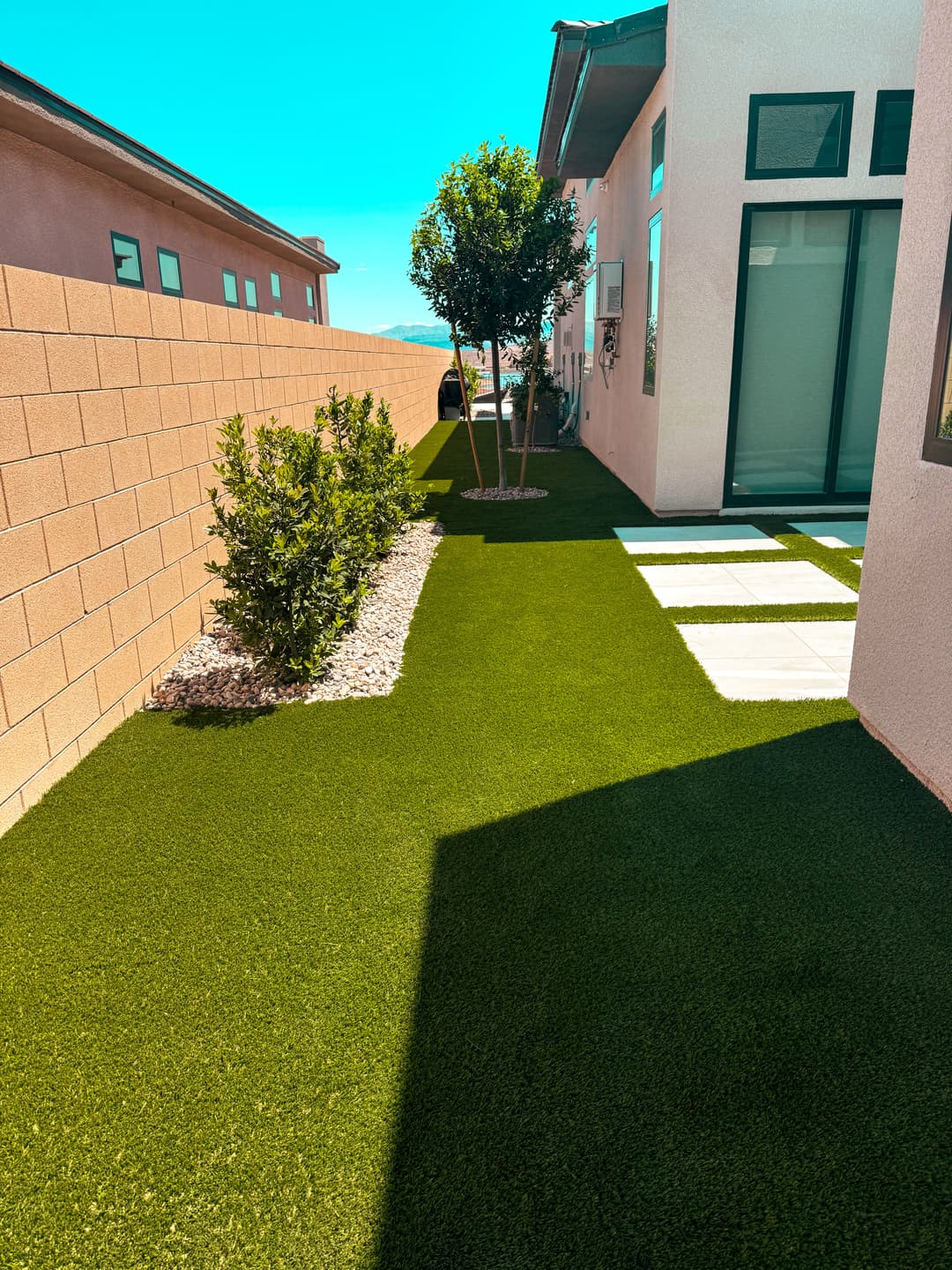 Lush green artificial turf path beside a modern home with decorative shrubs and stepping stones.