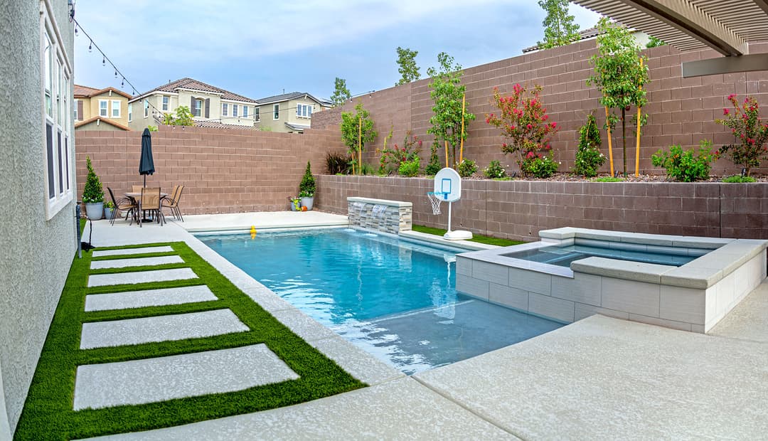 Modern backyard with pool, spa, and seating area surrounded by greenery and stone walls.